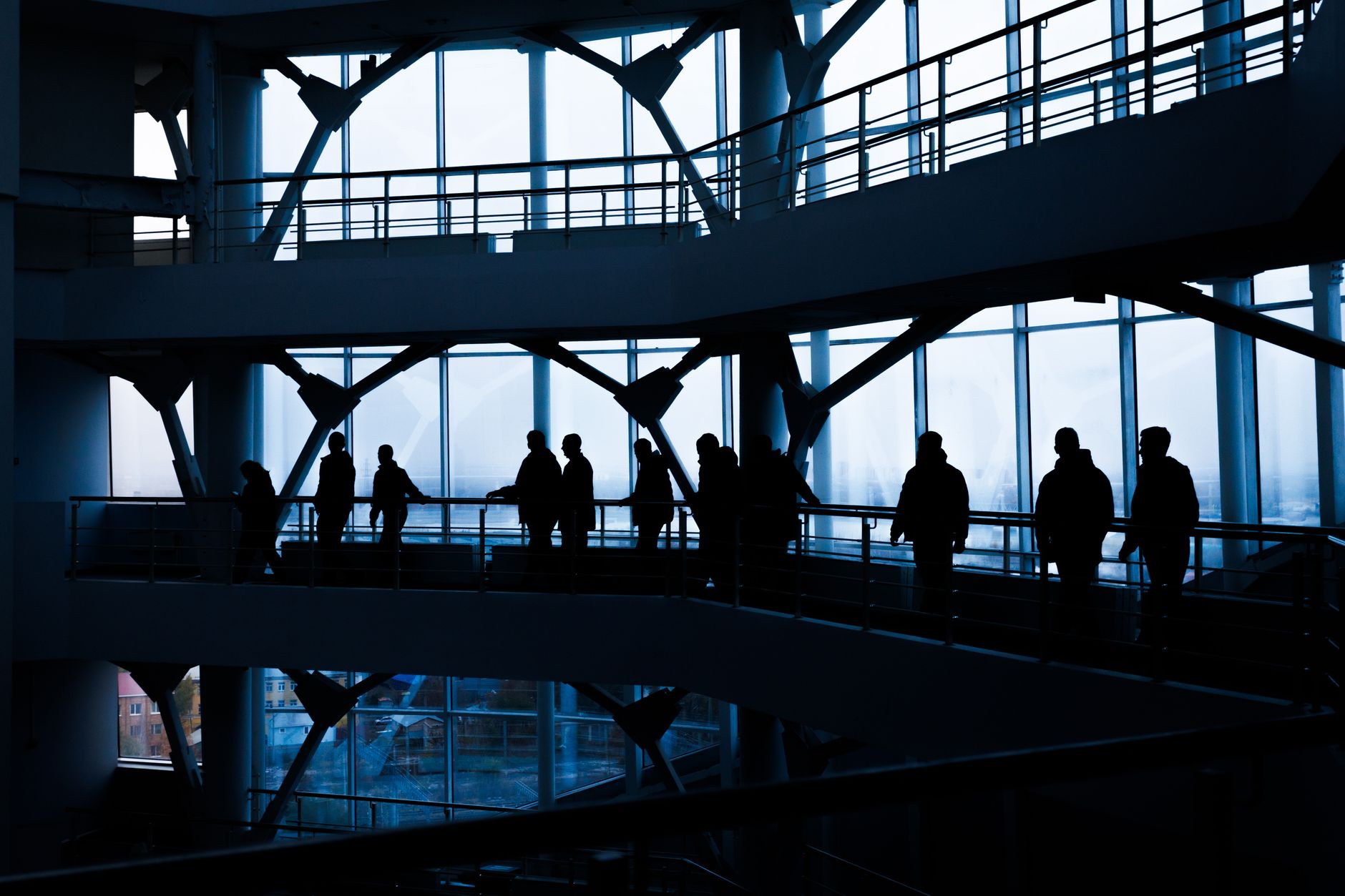 Silhouettes of people walking in a modern architectural building with large windows. — 3 Ways That A VNA Forklift Benefits Yo
