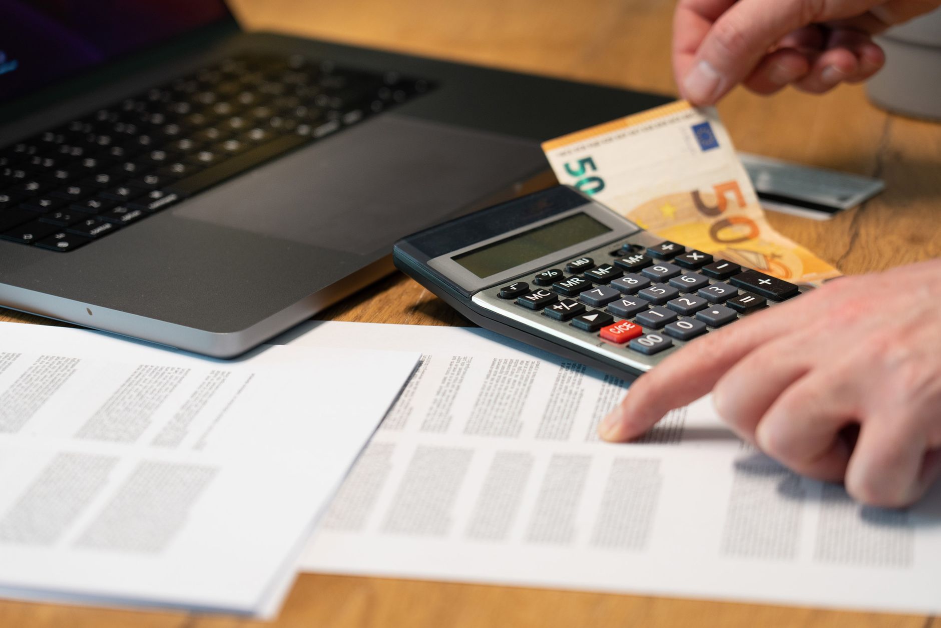 Close-up of hands using calculator with euro notes and laptop on desk. — 7 Unique Facilities of Mobile Banking Apps for Bette