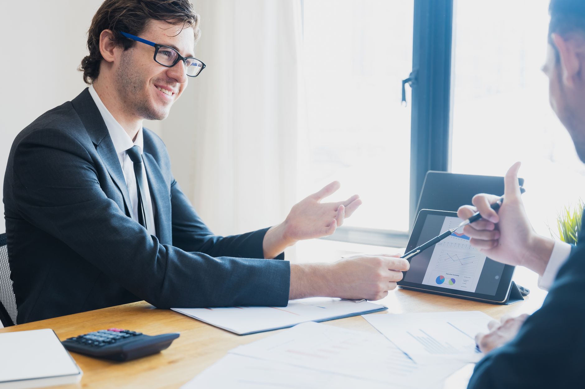 Two businessmen in formal attire discussing a business report in an office setting with a tablet. — Apply for an EMI Card Onl