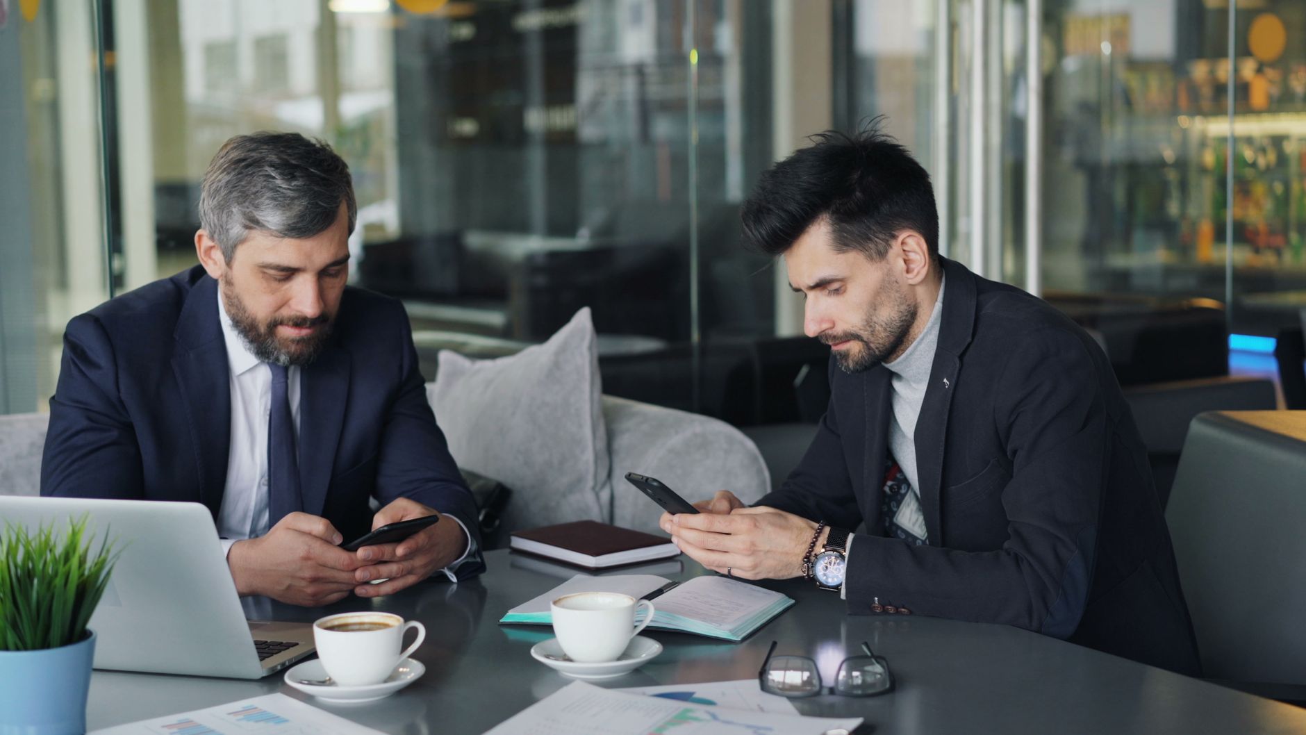 Two businessmen in a cafe working on smartphones and laptops, engaged in a meeting. — Auckland Advantages: 4 Reasons To Base