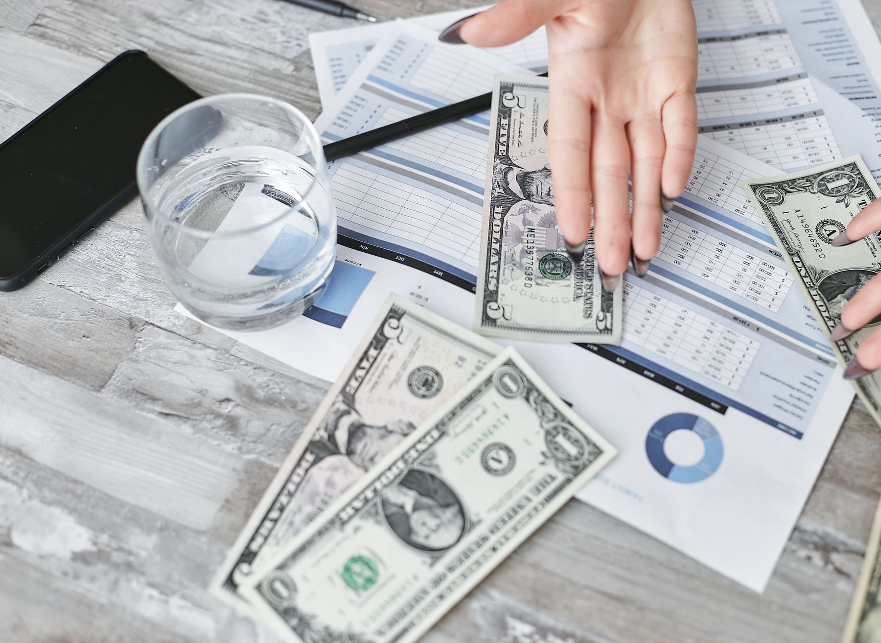 A top view of financial documents with dollar bills and a glass of water, emphasizing budgeting. — Can you make a profit by t