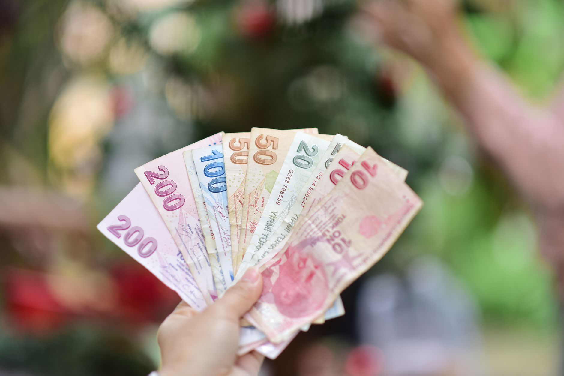 A hand holding multiple Turkish Lira banknotes in an outdoor setting, showcasing various denominations. — Can You Play Tirang