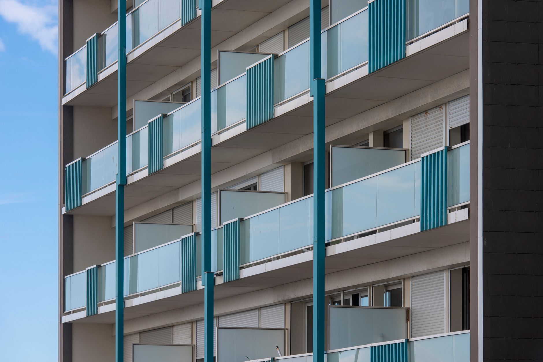 Exterior view of a modern apartment building with multiple blue balconies, showcasing contemporary architectural design. — Co
