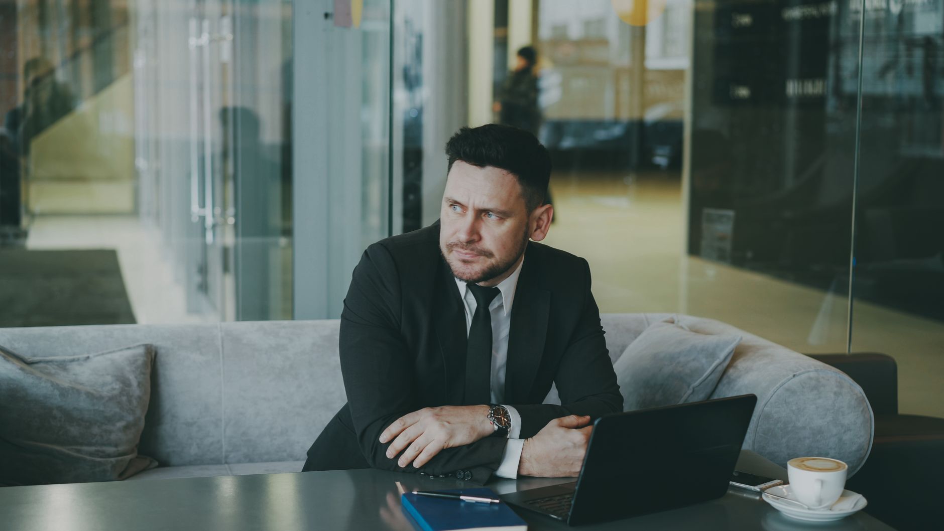 A businessman in a suit sits thoughtfully in an office lounge with a laptop. — Entrepreneurship - Who's An Entrepreneur?