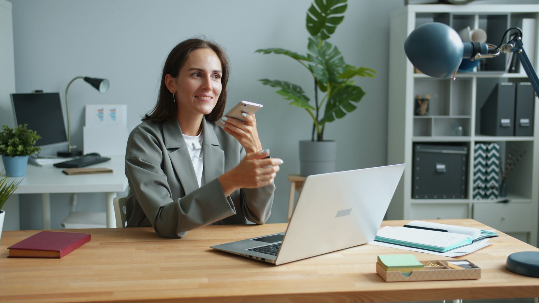 Confident businesswoman using smartphone and laptop in modern office setting. — Film Translation And Subtitling: Find Out How