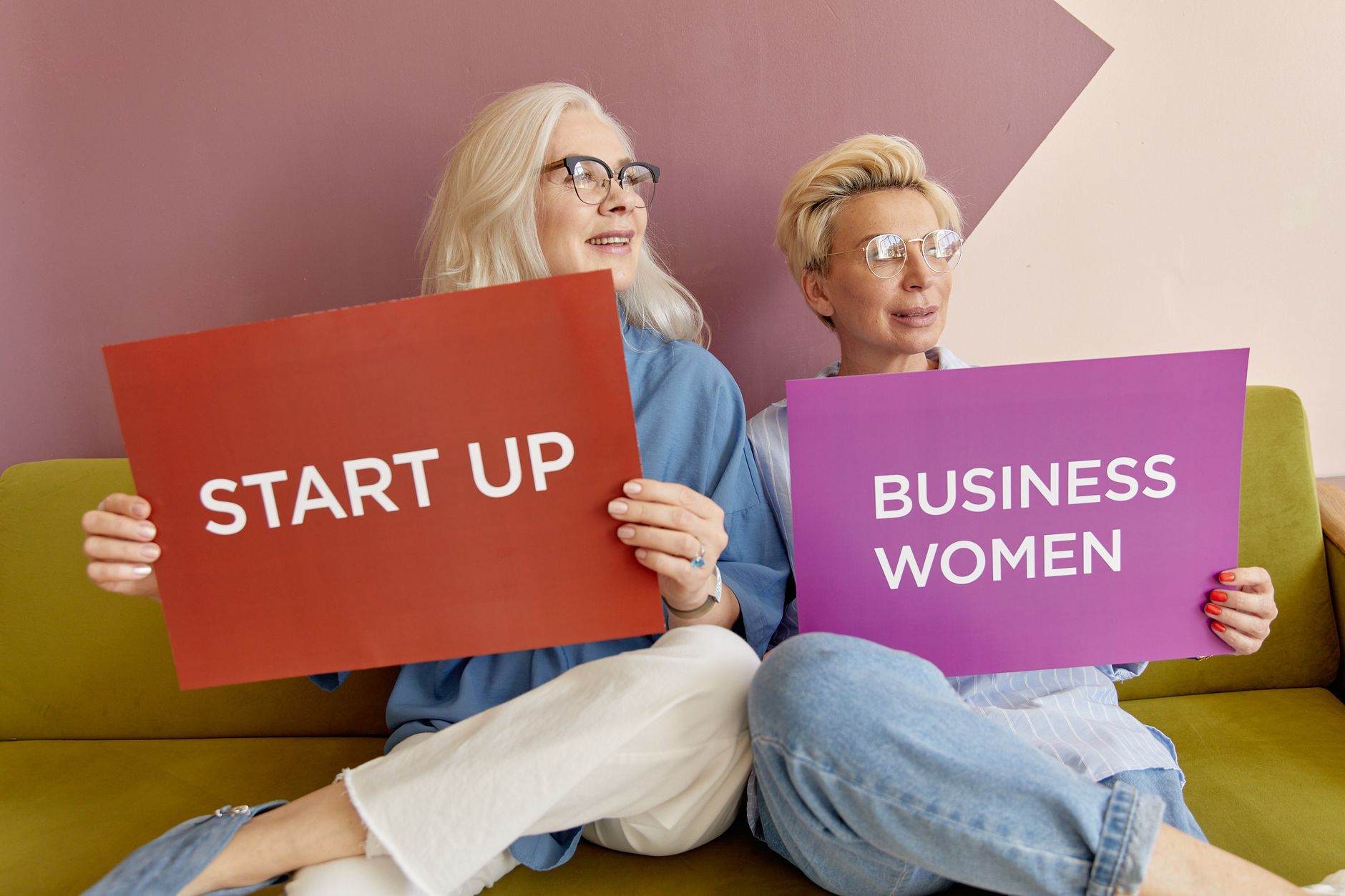 Two women on a sofa holding signs promoting startup and business women. — Finding the best DUI attorney: Check these tips!