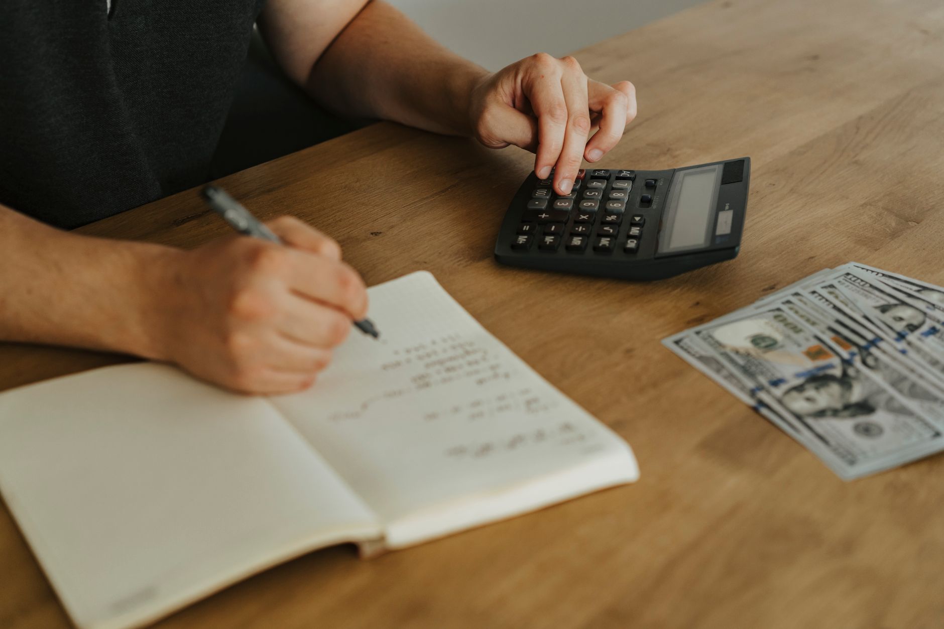 Close-up of hands using a calculator with notebook and cash on a wooden table. — Get The Money You Need With Slick Cash Loan
