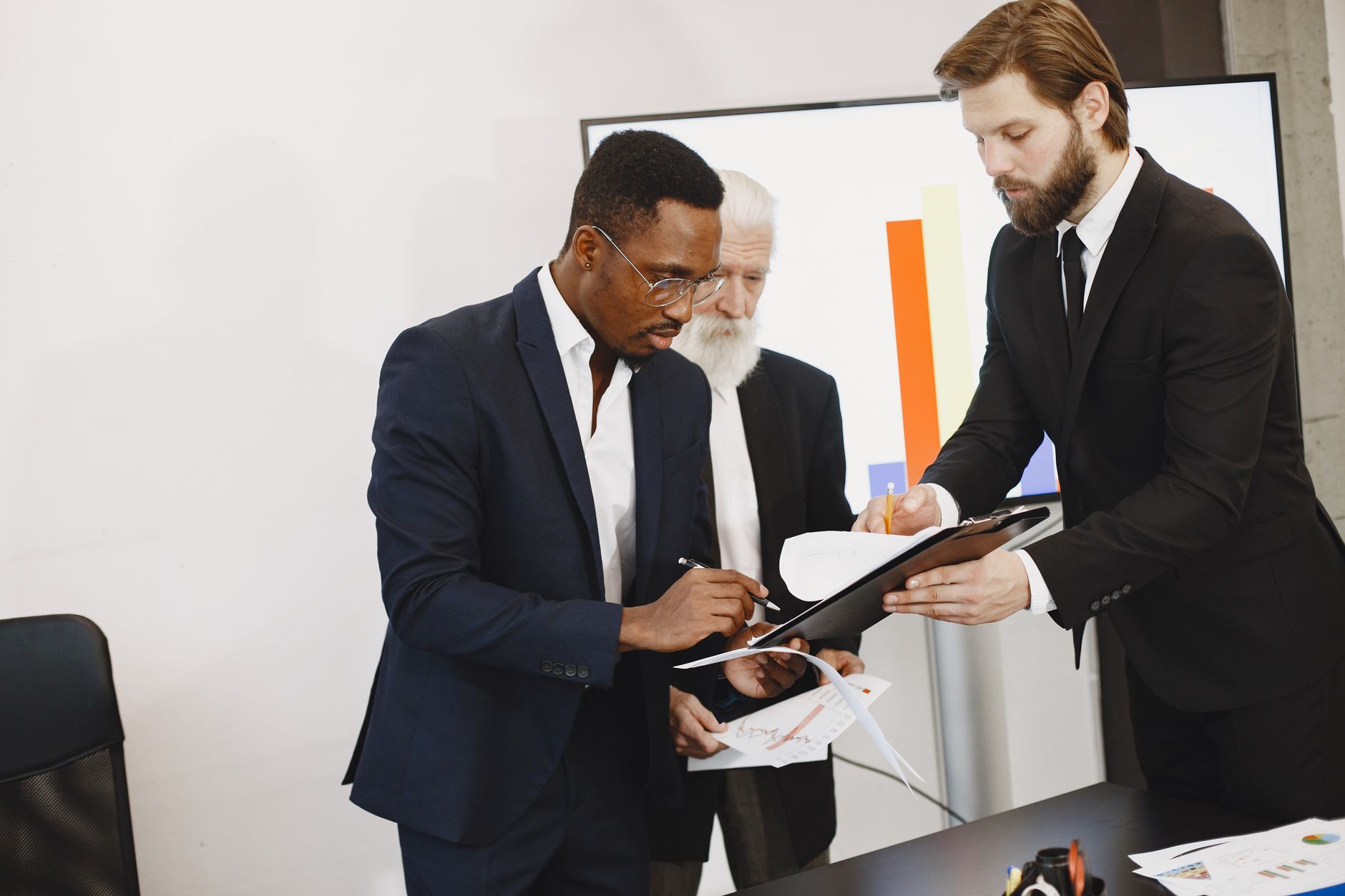 Three businessmen engaged in document signing in a modern office setting. — Get the Traffic Faster For Your Pearl Jewelry Bus