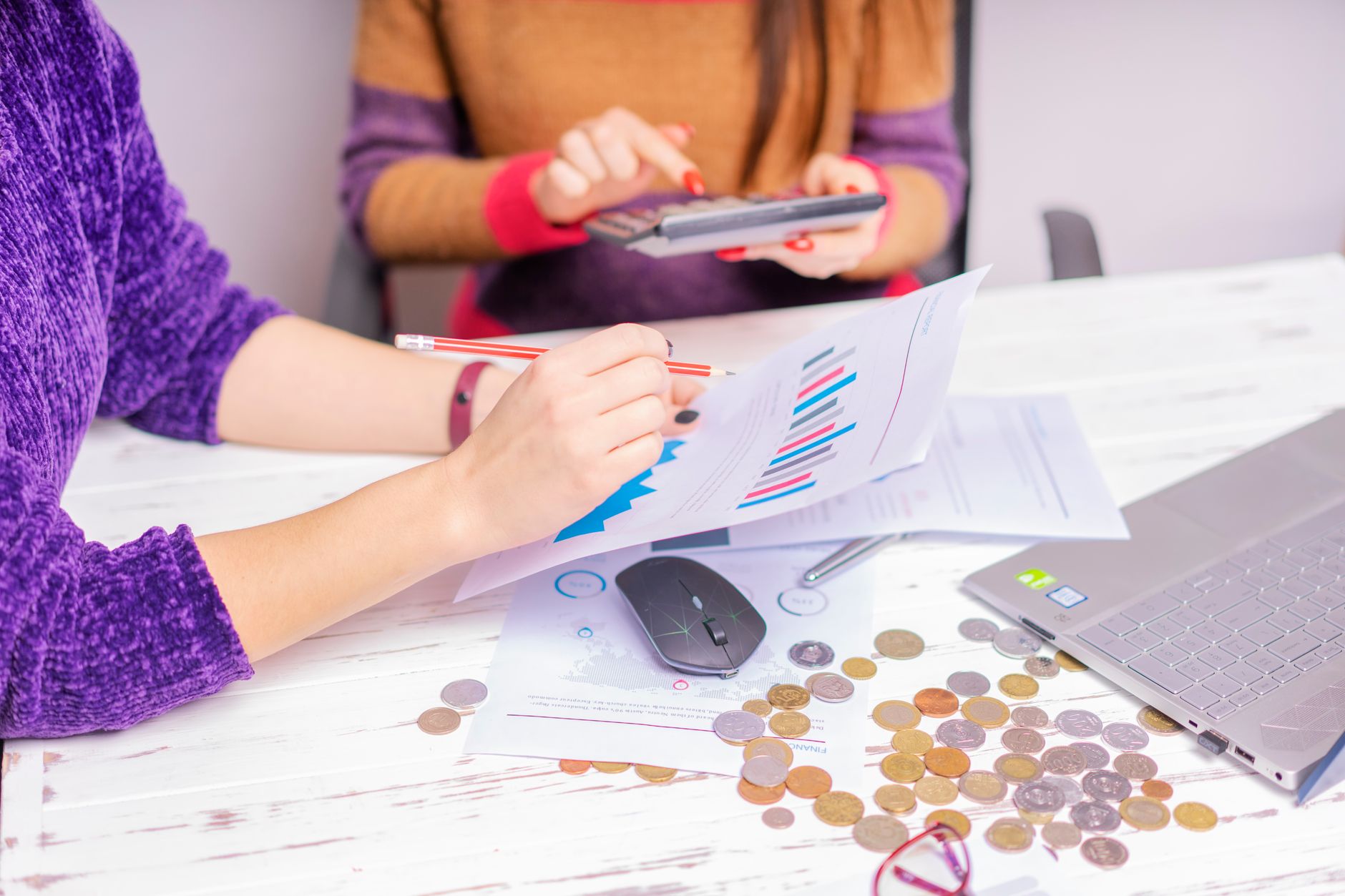 Two women analyzing financial charts with a laptop and coins on desk in an office setting. — How can a loan app help you obta