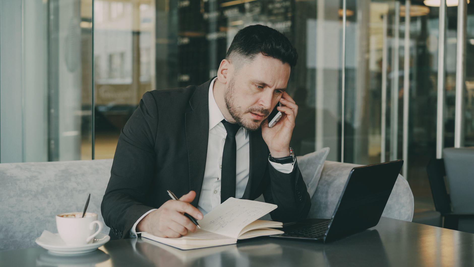 Businessman talks on phone while writing notes in a modern cafe. — How Corporate Meal Delivery Helps Employees?