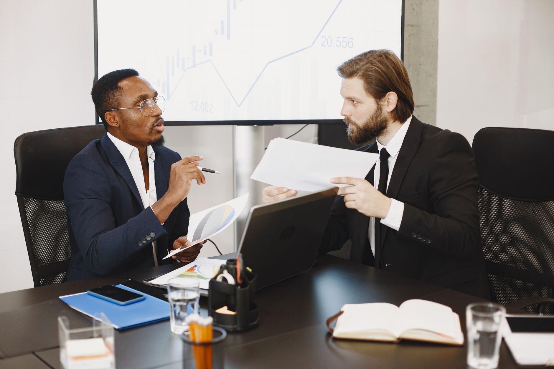 Two business professionals engaged in a planning meeting, discussing documents in a modern office setting. — How Much Do You