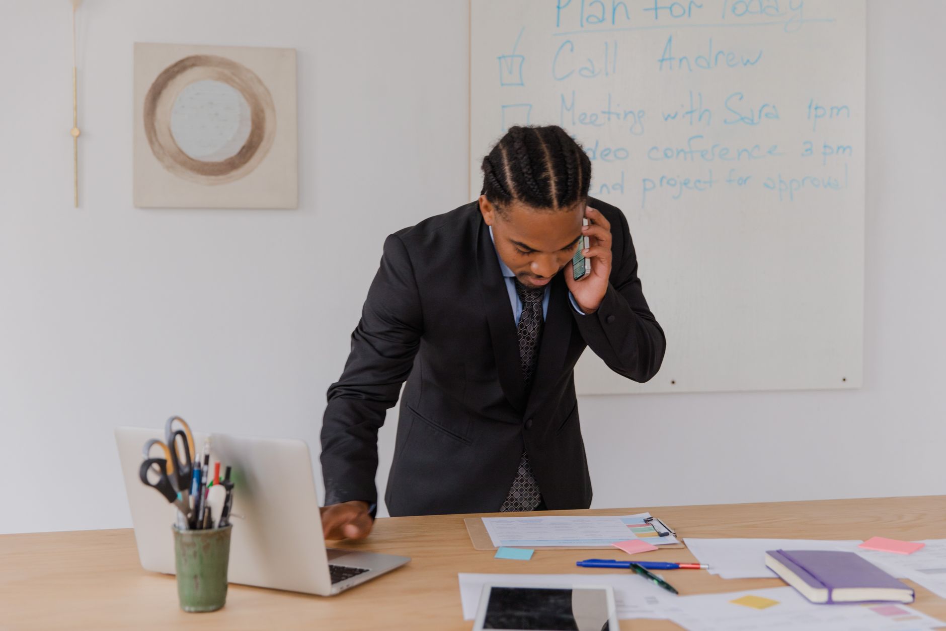Professional businessman multitasking with phone and laptop at office desk, surrounded by documents. — How to Connect Roku to