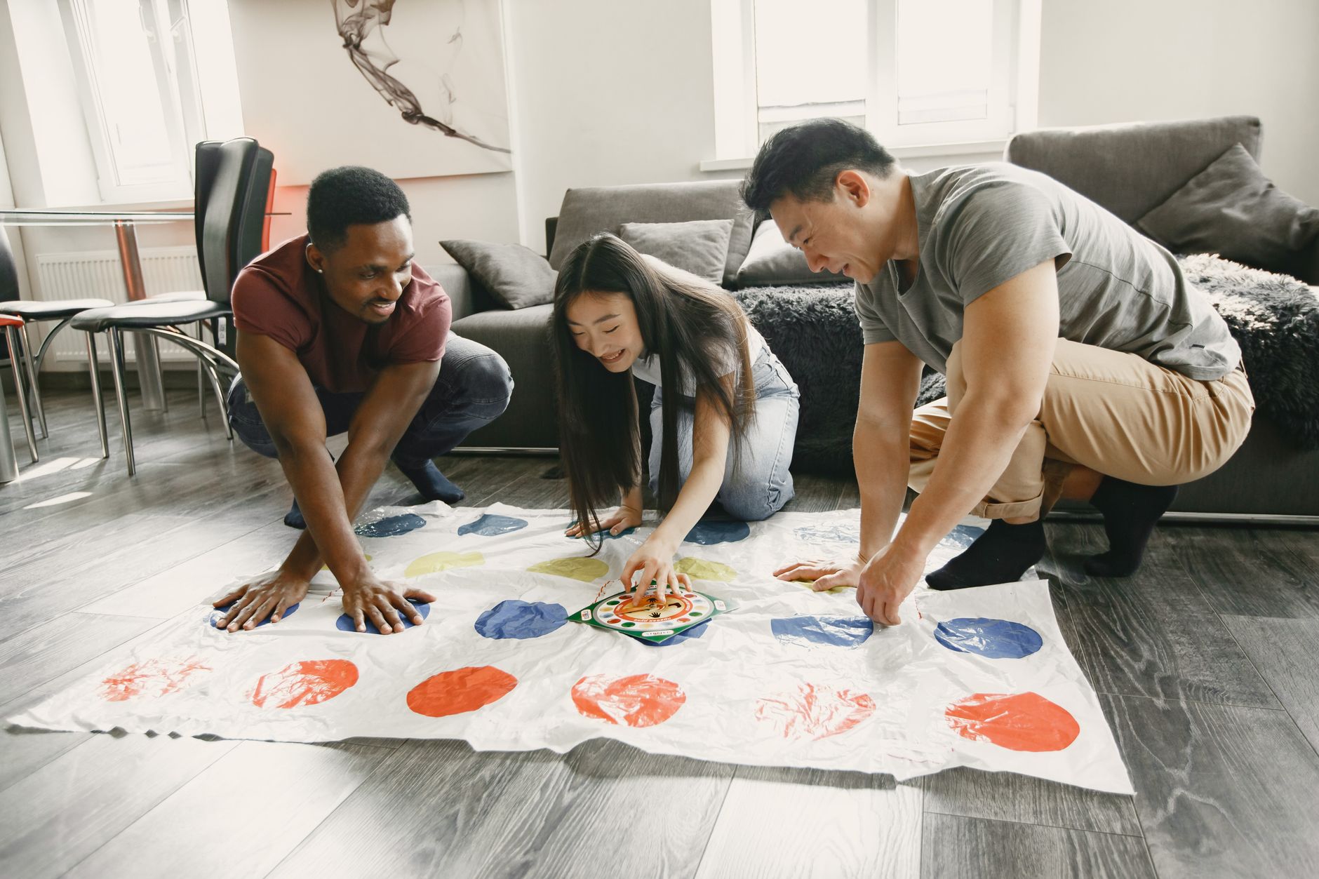 Three diverse friends enjoy a lively game of Twister in a cozy living room. Perfect for lifestyle and leisure themes. — How t