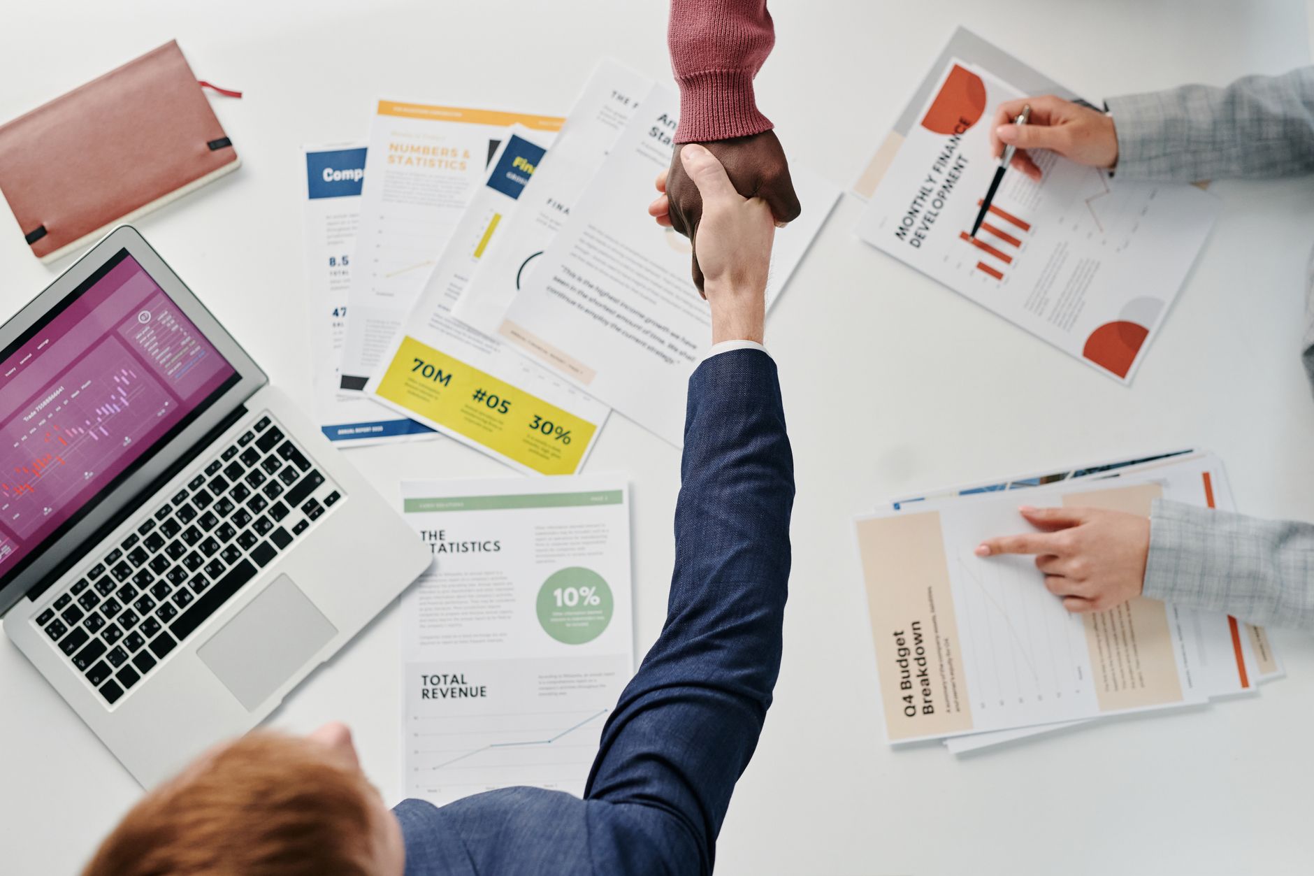 Business professionals engaging in a handshake over a desk filled with financial documents and a laptop. — How to work for yo