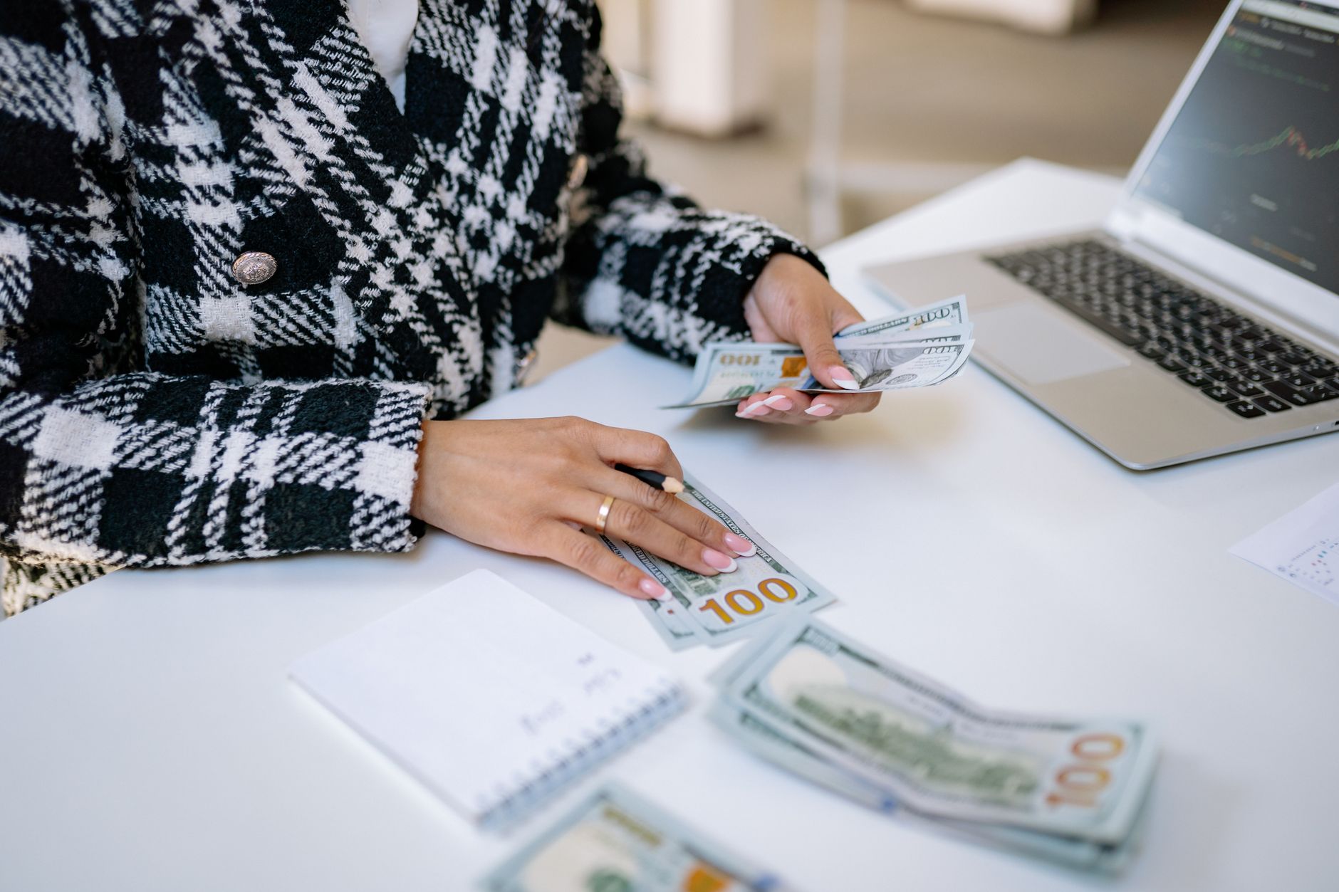 Close-up of a woman counting hundred-dollar bills at a desk with a laptop, focusing on finance and work. — IMPORTANT THINGS T