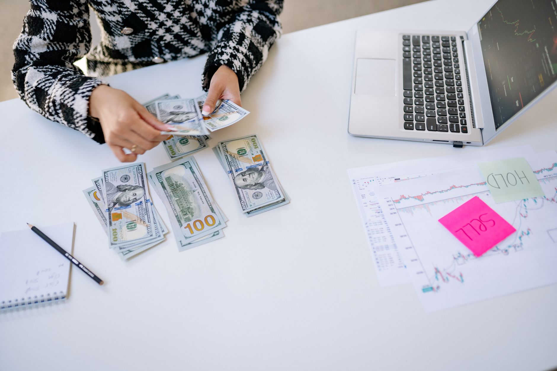 Person counting cash next to laptop and stock market charts on a white table. — No Credit Check Loans and What is Required