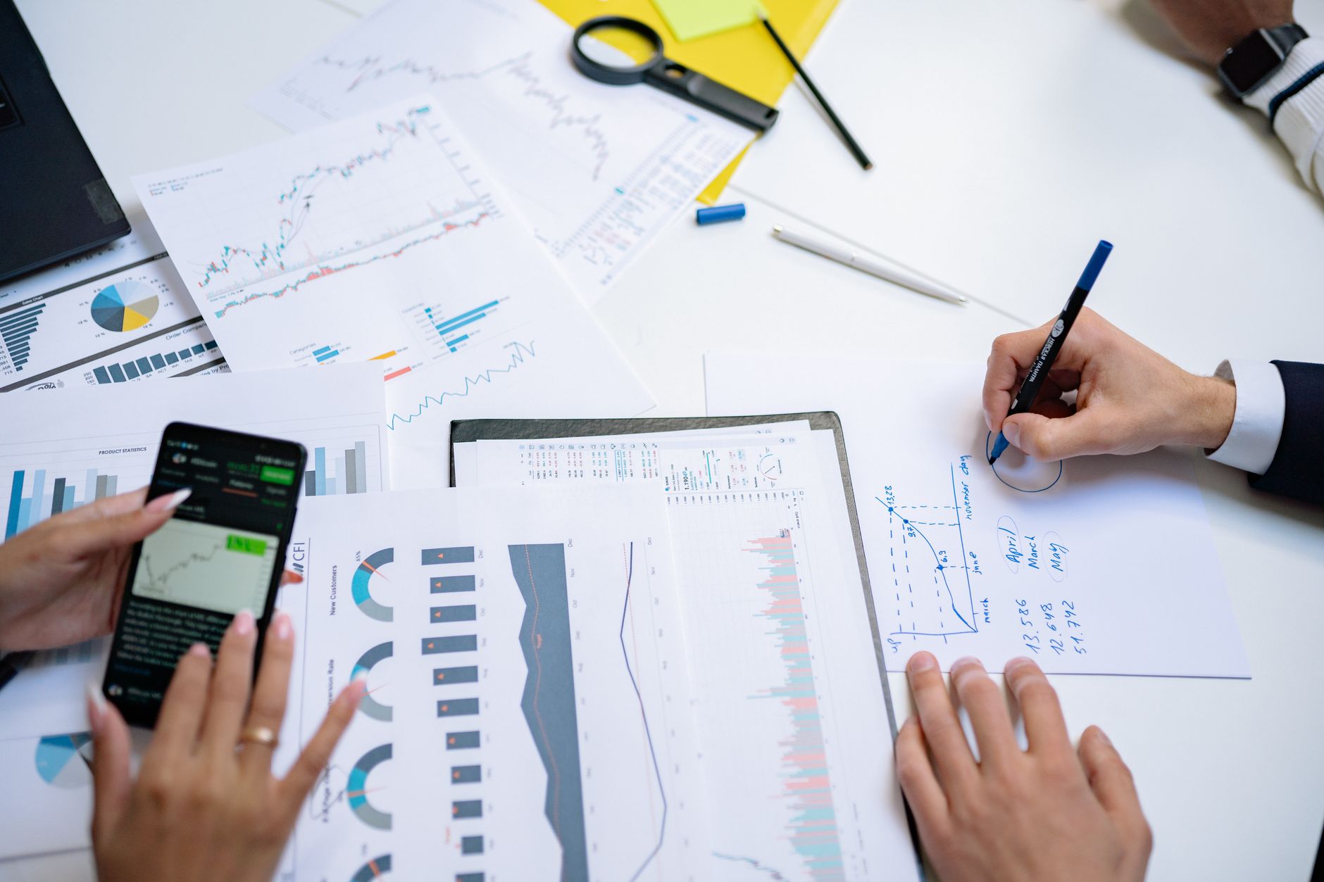 Colleagues collaborating on financial charts and graphs using mobile and paper documents in the office. — On-Demand Massage L