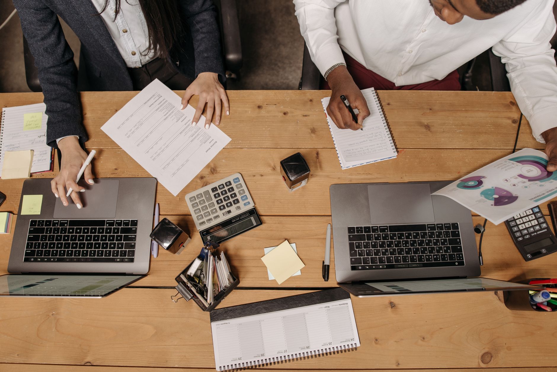 High-angle view of professionals working collaboratively with laptops and documents in an office. — Perfection in The Running