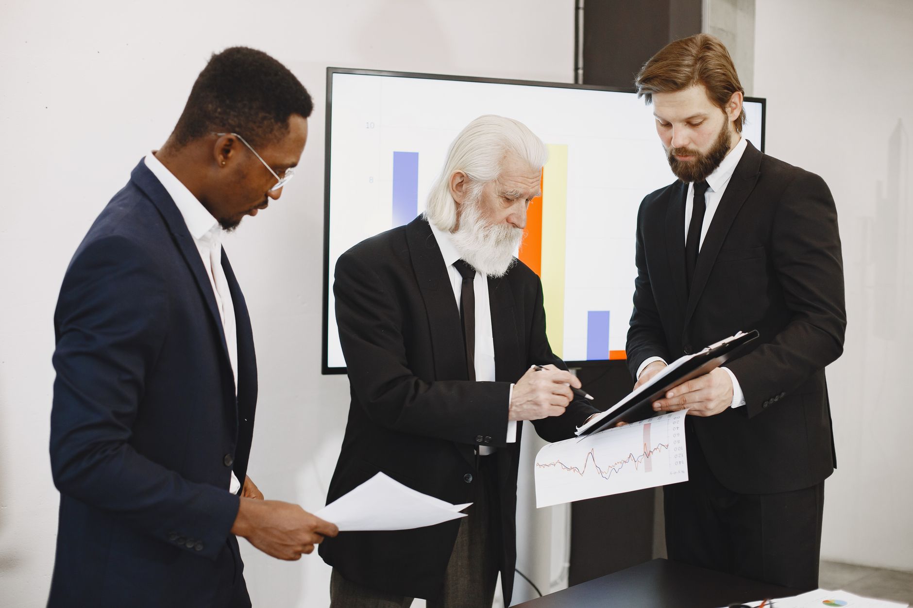 Three businessmen in suits reviewing reports and graphs during an office meeting. — Private Investigator Melbourne Delivering