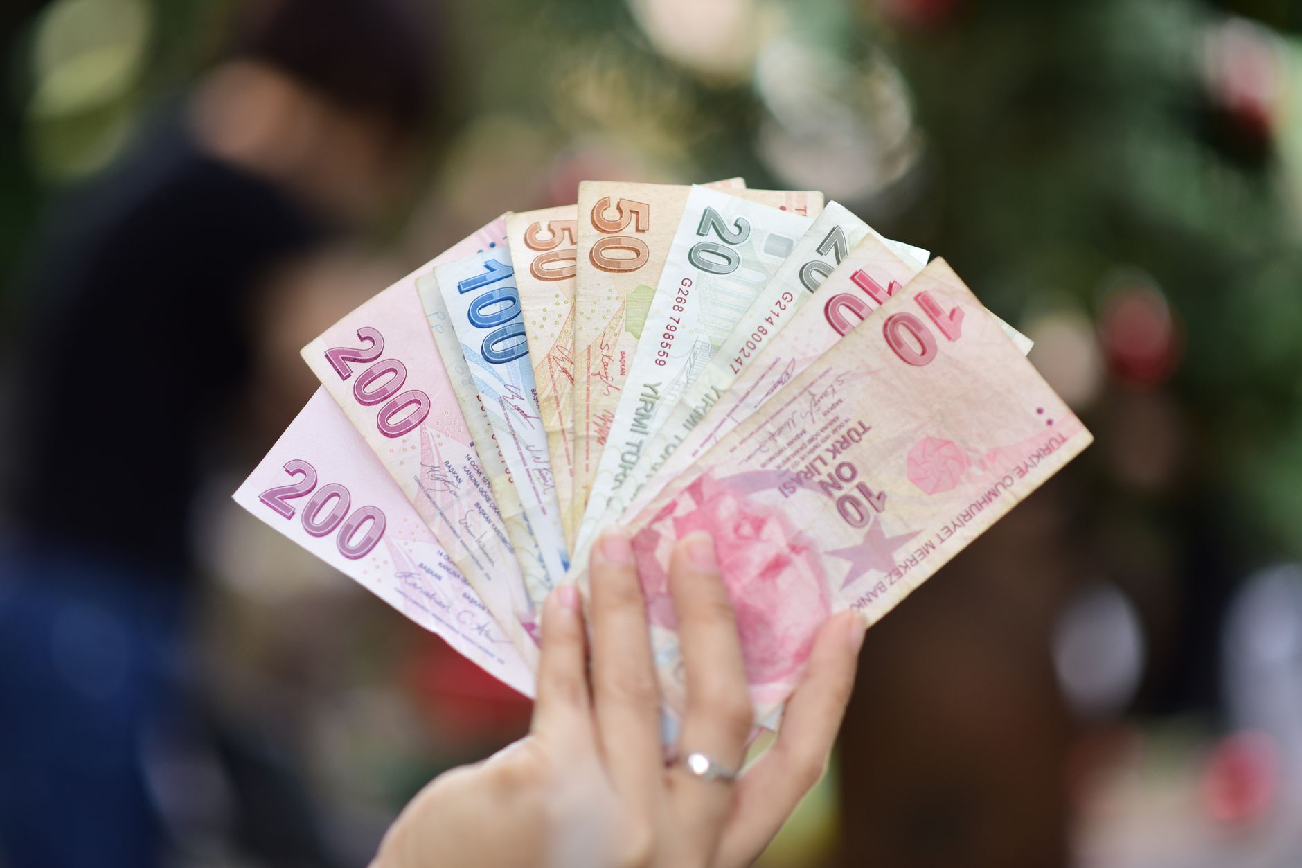 Hand holding multiple denominations of Turkish Lira banknotes outdoors. — RNG or Live Dealer? Choosing the Right Experience o