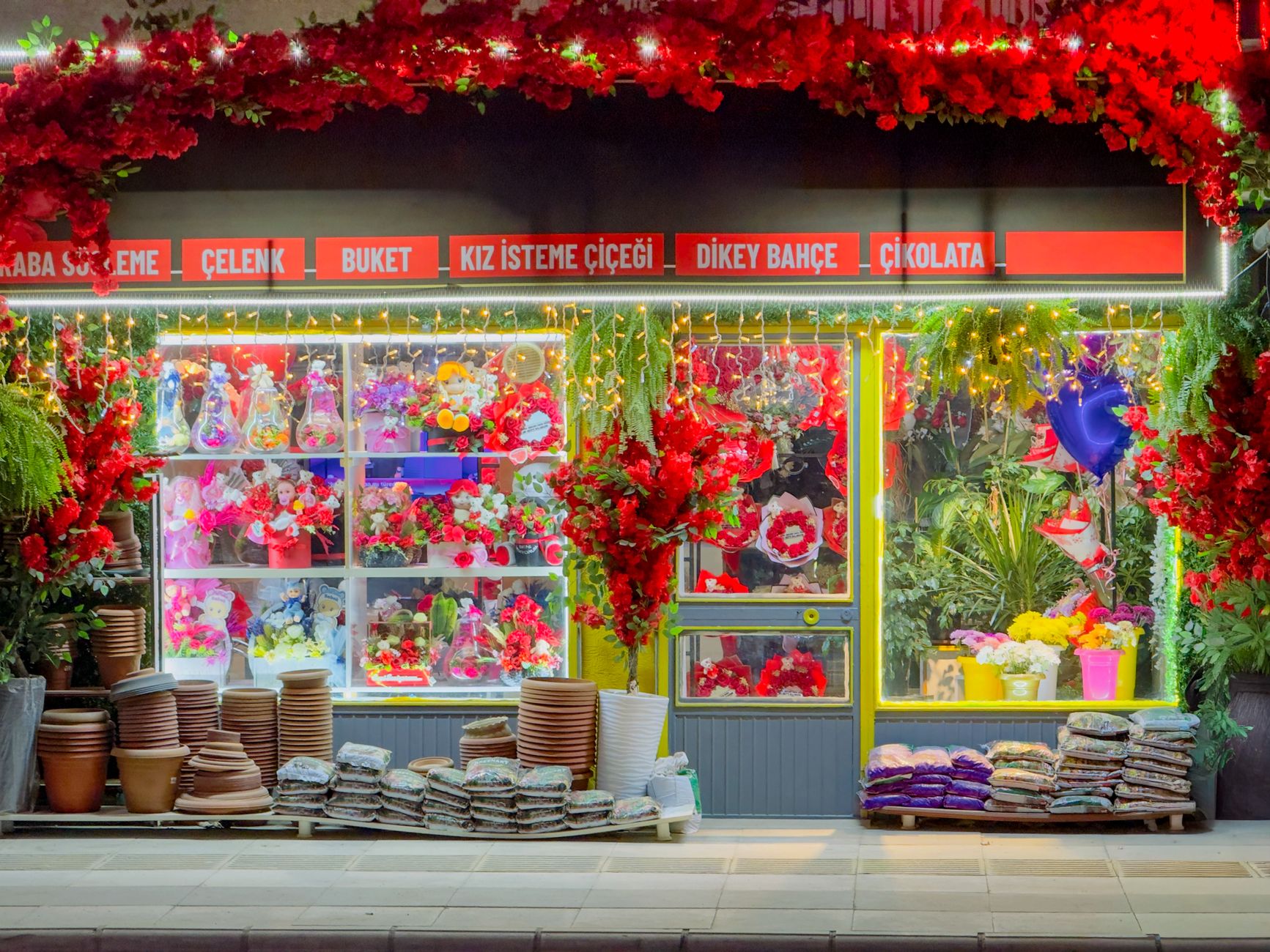 A vibrant floral shopfront in Elâzığ, Türkiye, illuminated at night with colorful flowers and decorative lighting. —