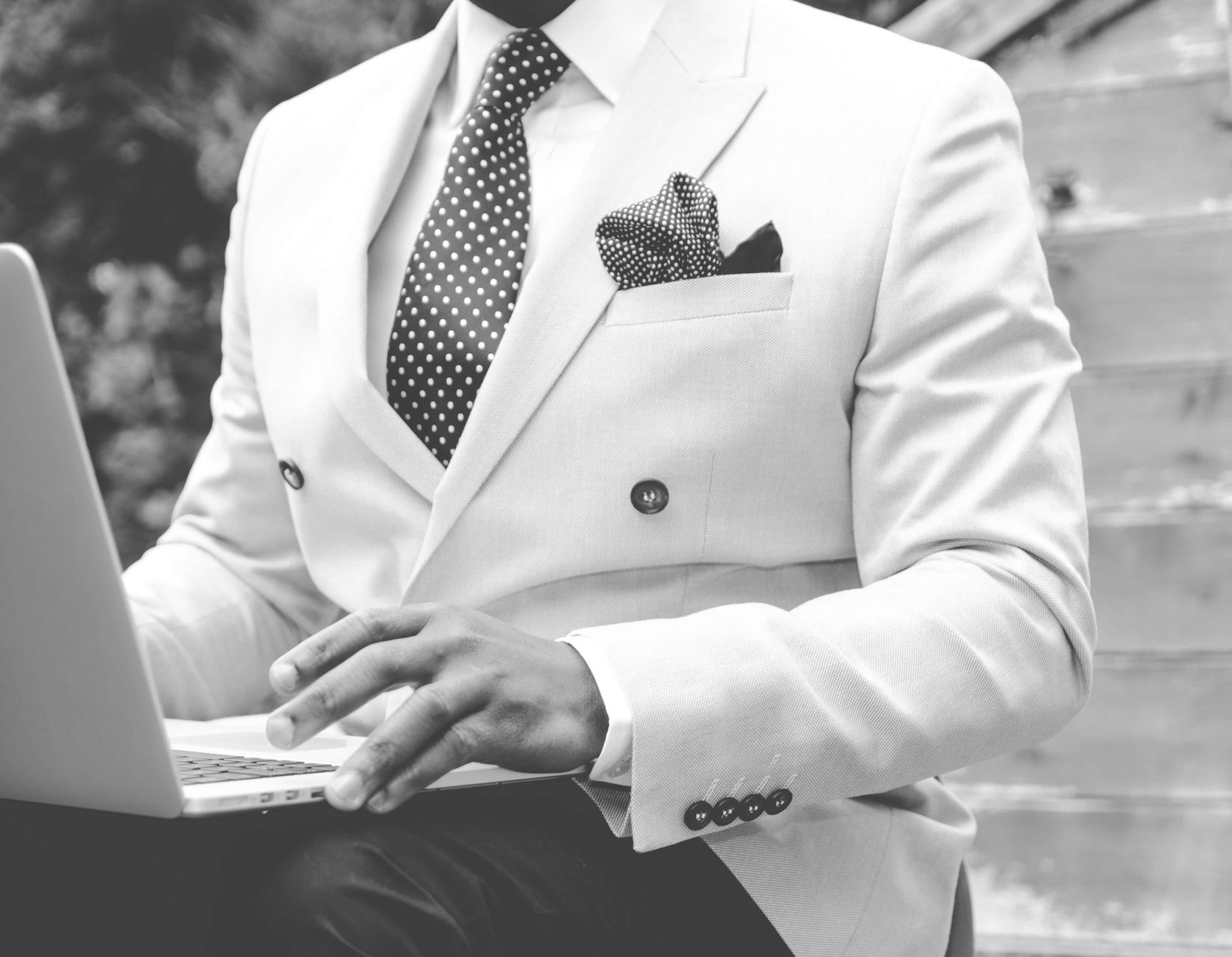 Black and white photo of a man in a suit typing on a laptop outdoors. — Ten Useful Techniques for Entrepreneurs While Creatin
