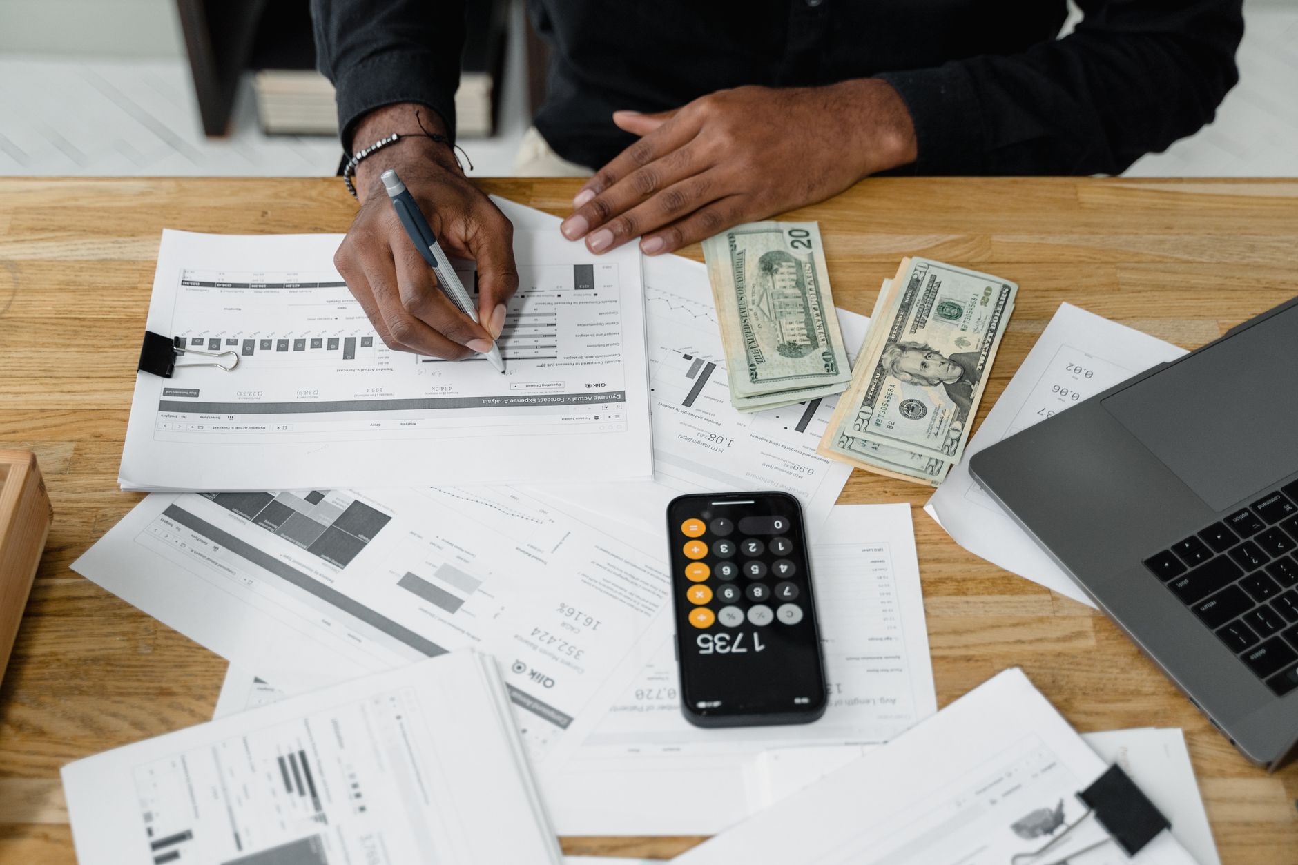 Man working on financial reports with calculator, money, and laptop on a desk. — The best stock trading sites in Hong Kong