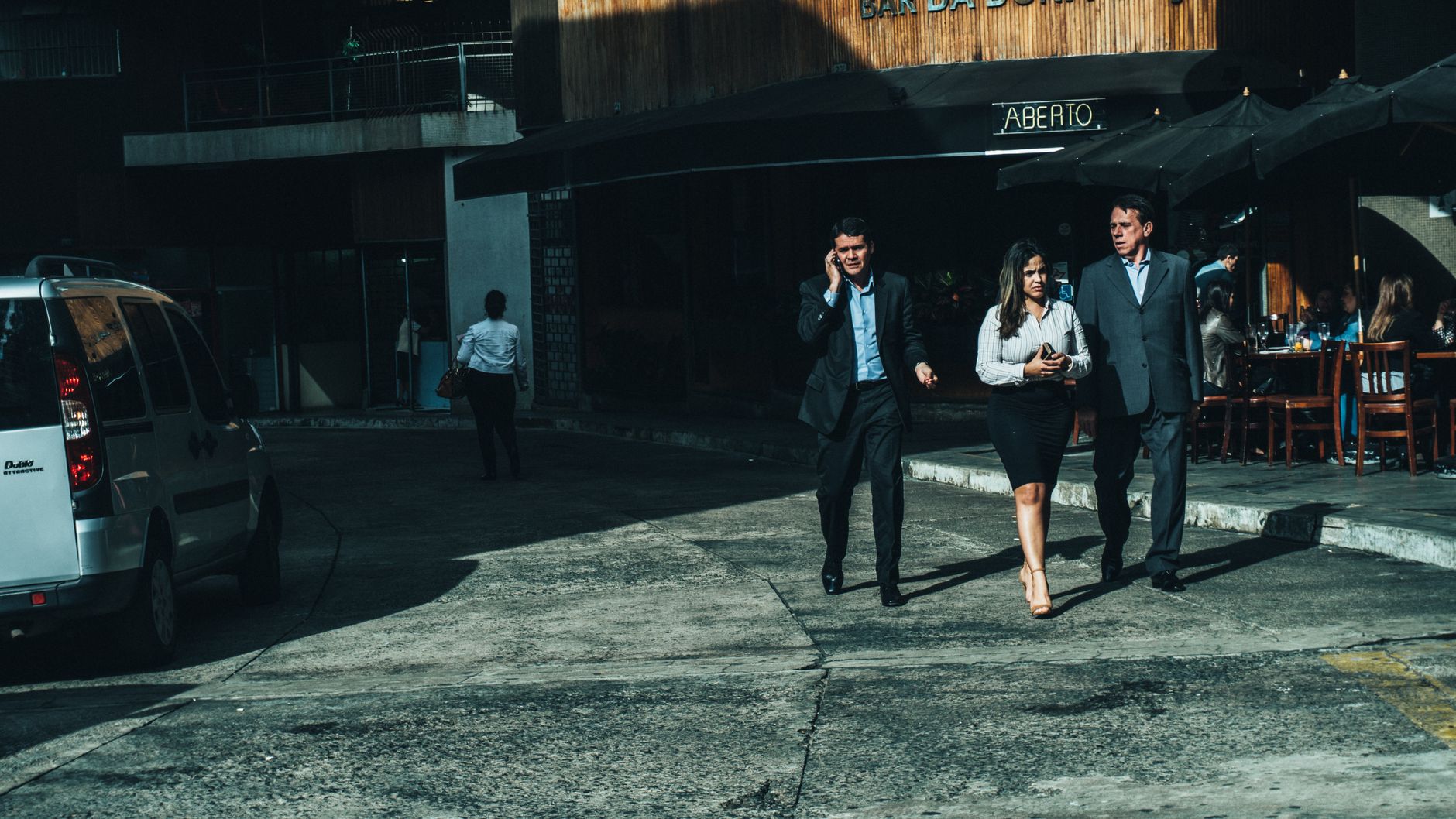 Three business professionals walk along a city street outside a cafe. — The Role of CFB Stream in Enhancing College Football