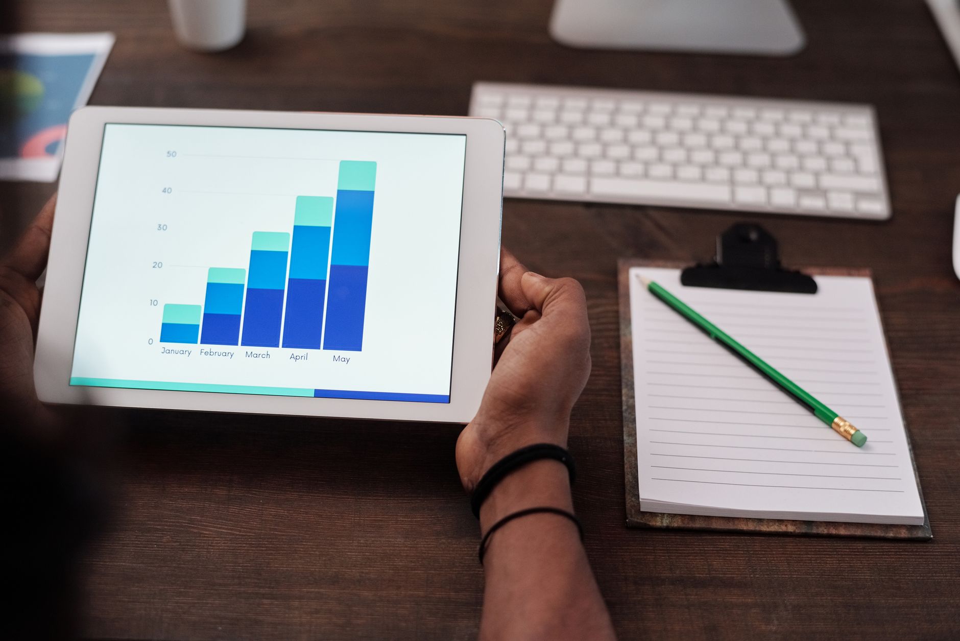 Close-up of a person holding a tablet showing growth charts on a wooden desk setup. — The Ultimate Guide to Web Design for We