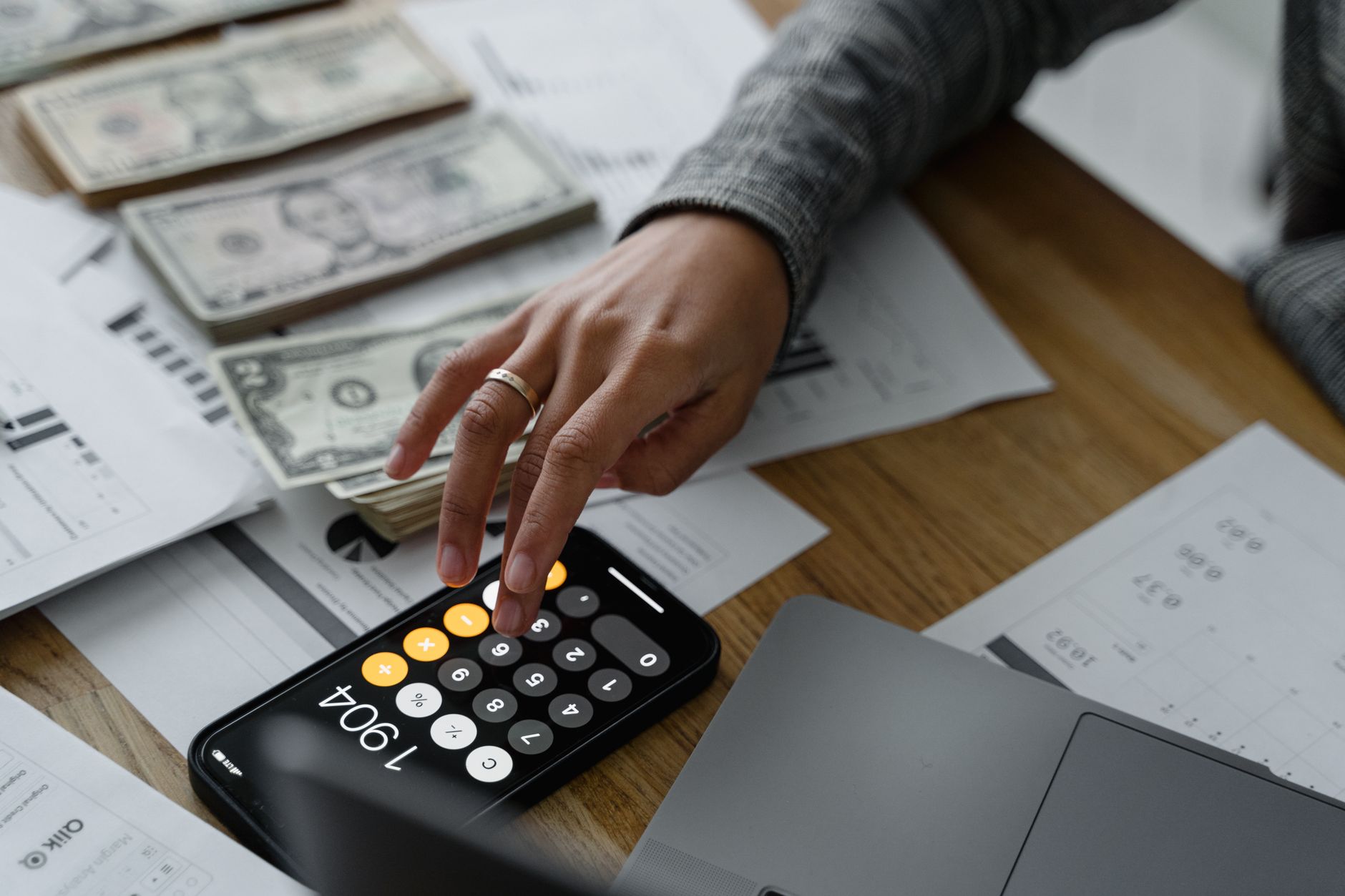 Close-up of a person using a smartphone calculator amid money and financial documents on a wooden table. — ULIP vs PPF - Wher