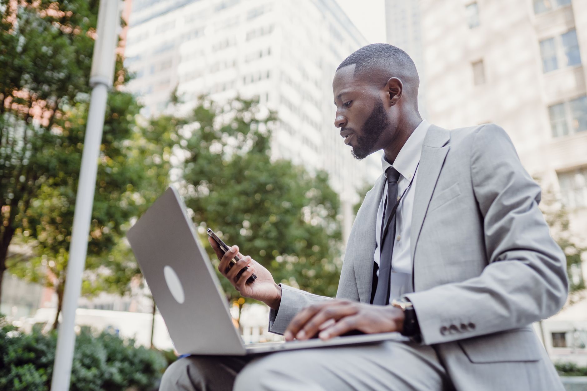 Businessman in a suit using a laptop and smartphone in an urban setting, blending technology with business. — What Should You