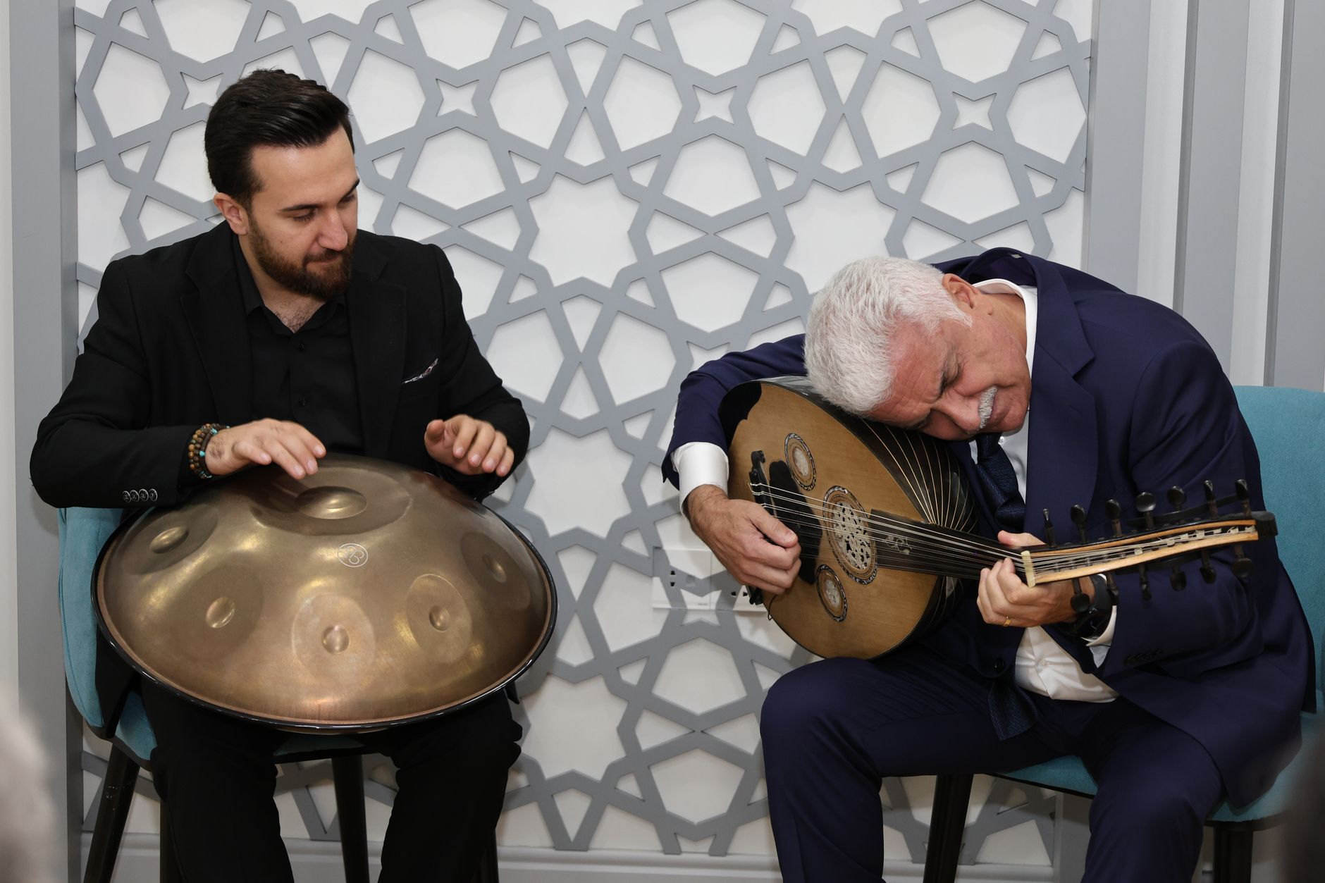 Two musicians playing oud and handpan in a cozy indoor setting, conveying cultural richness and musical harmony. — Why build